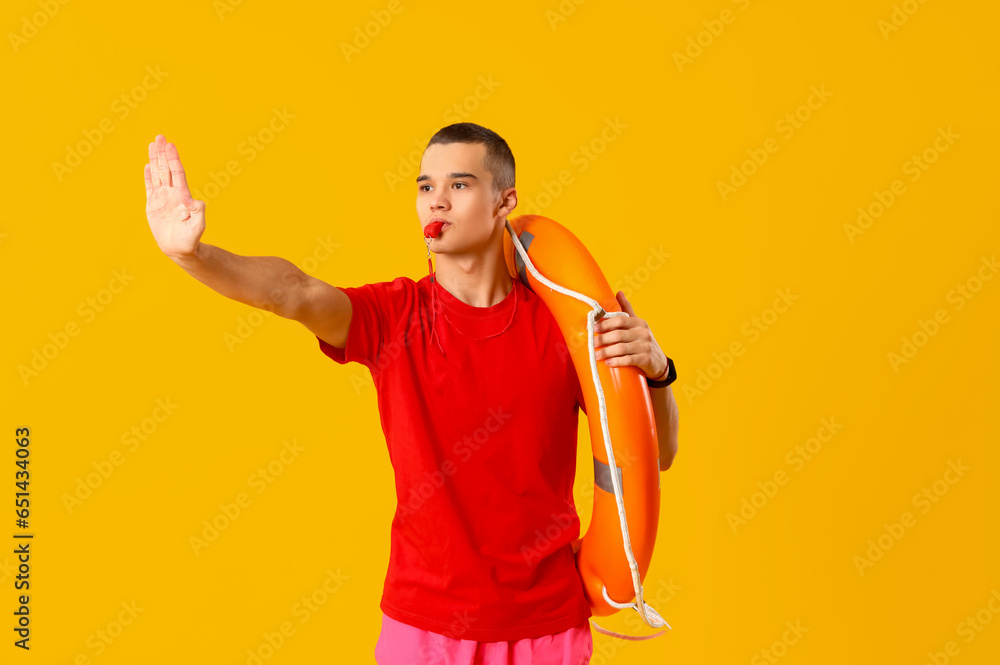 Male lifeguard with ring buoy whistling on yellow background