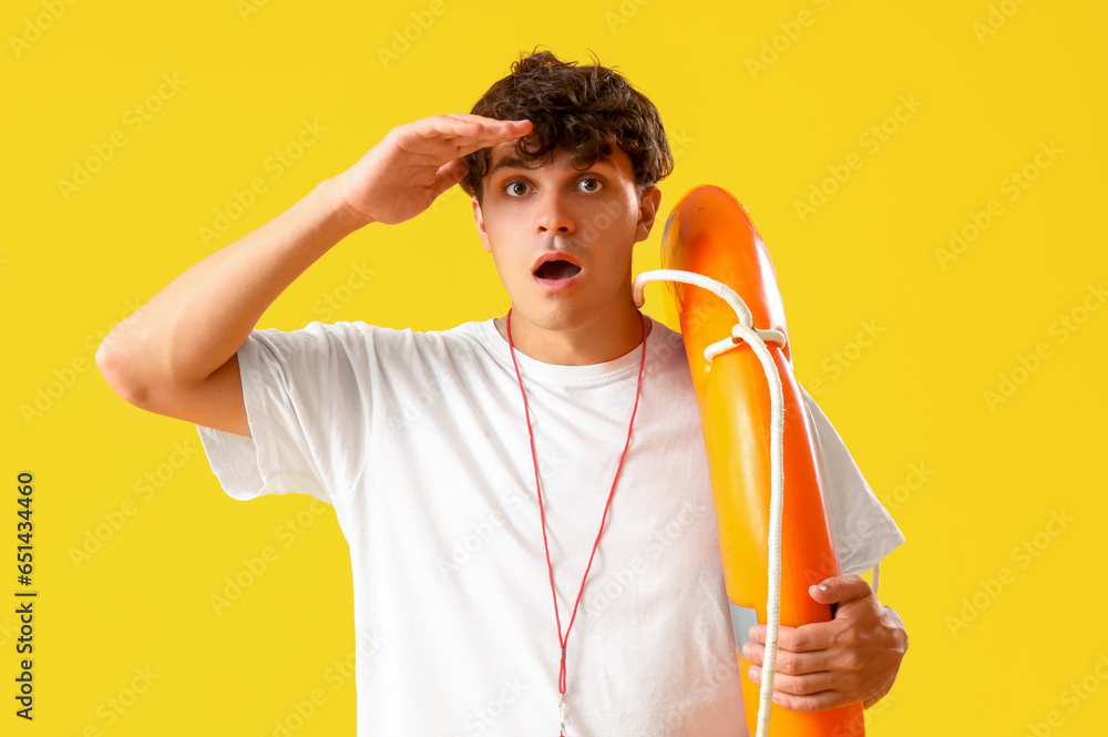 Shocked male lifeguard with ring buoy on yellow background