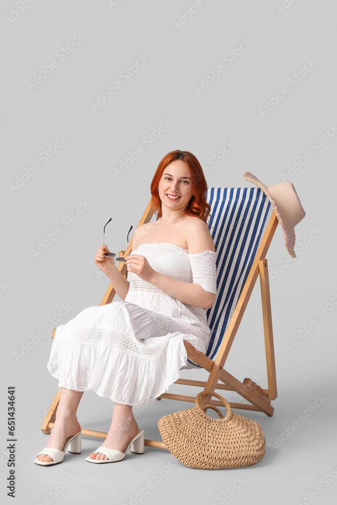 Young woman with sunglasses relaxing in deck chair on light background