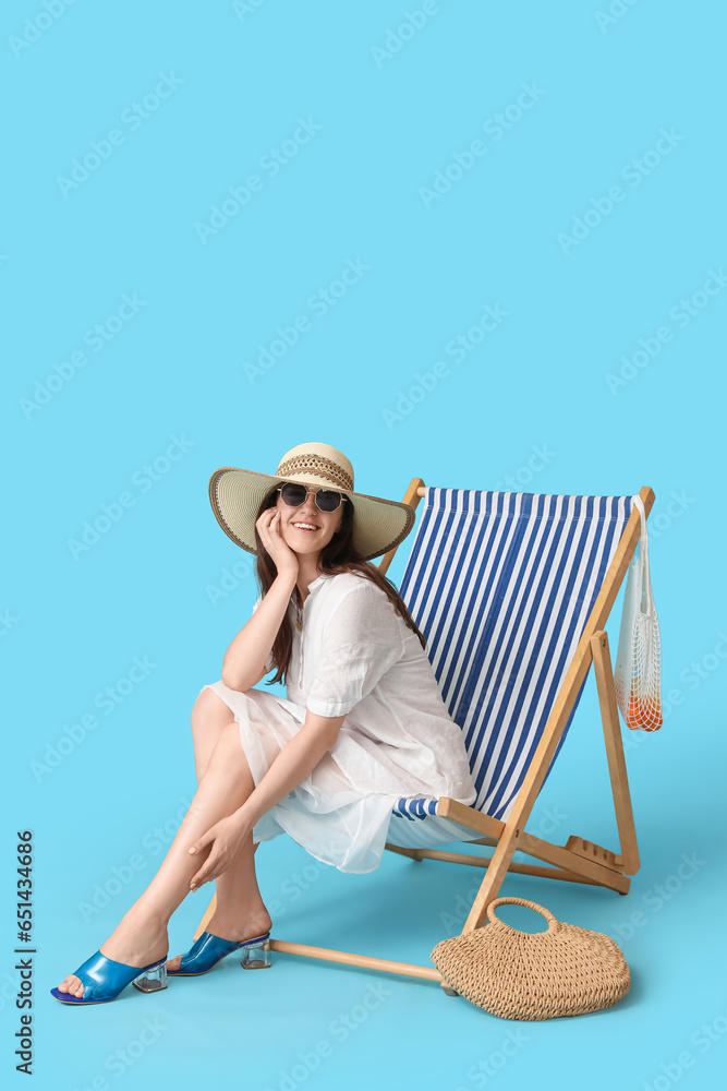 Young woman relaxing in deck chair on blue background