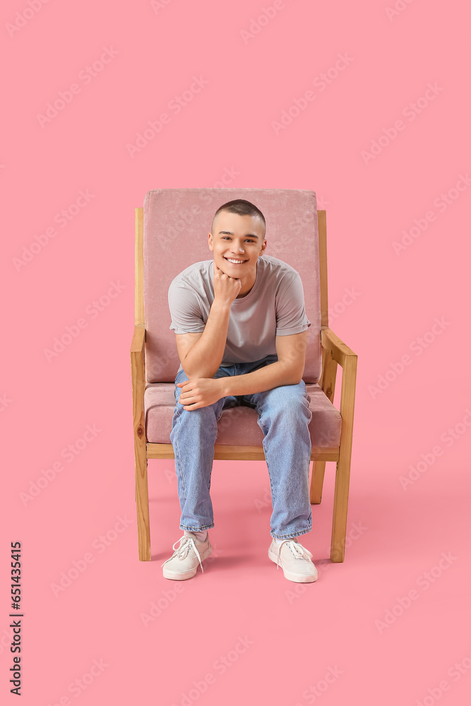 Happy young man sitting on chair against pink background