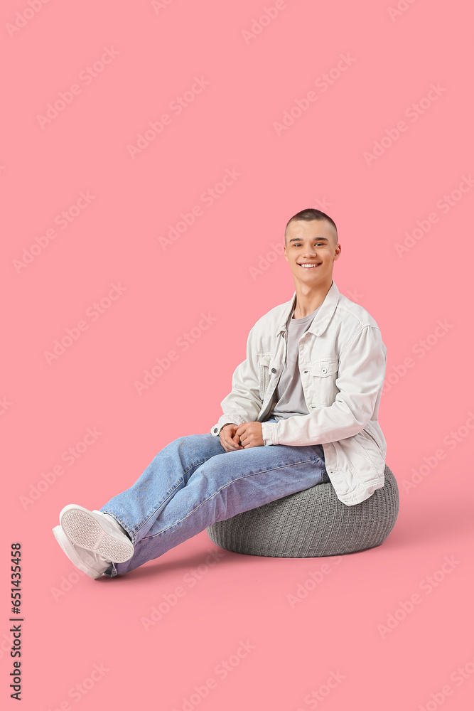 Happy young man sitting on ottoman against pink background