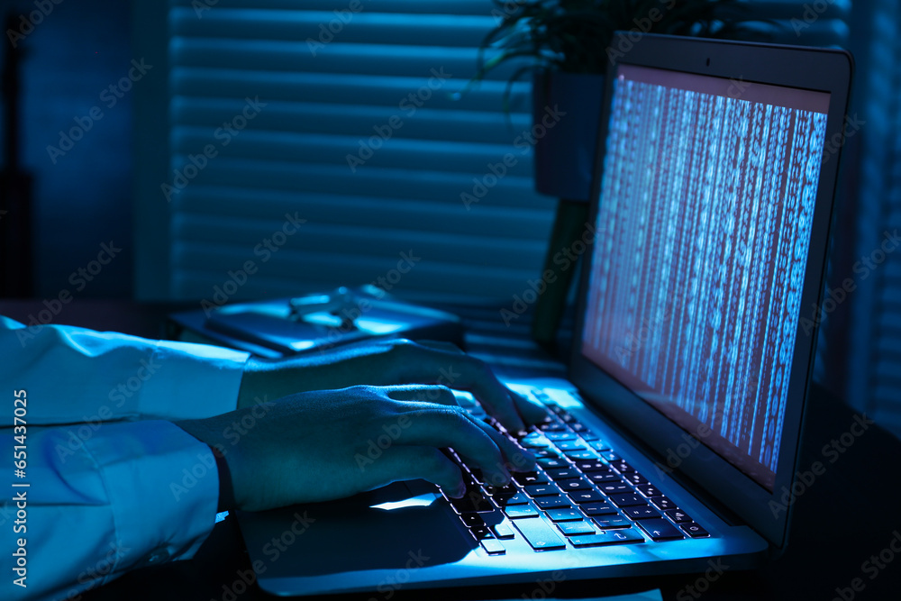 Female programmer typing on laptop keyboard at night in office, closeup