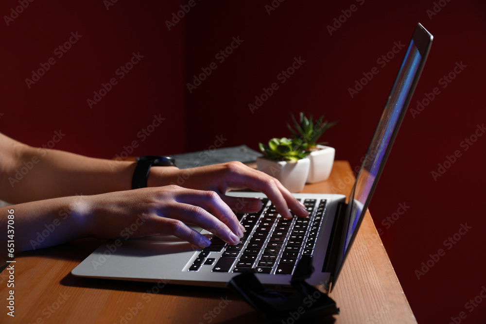 Female programmer typing on laptop keyboard at night in office, closeup