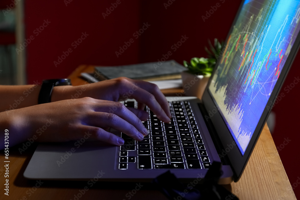 Female programmer typing on laptop keyboard at night in office, closeup