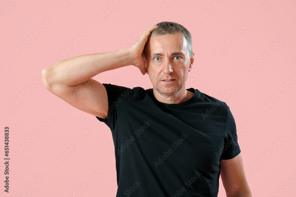 Portrait of shocked mature man holding his head on pink background