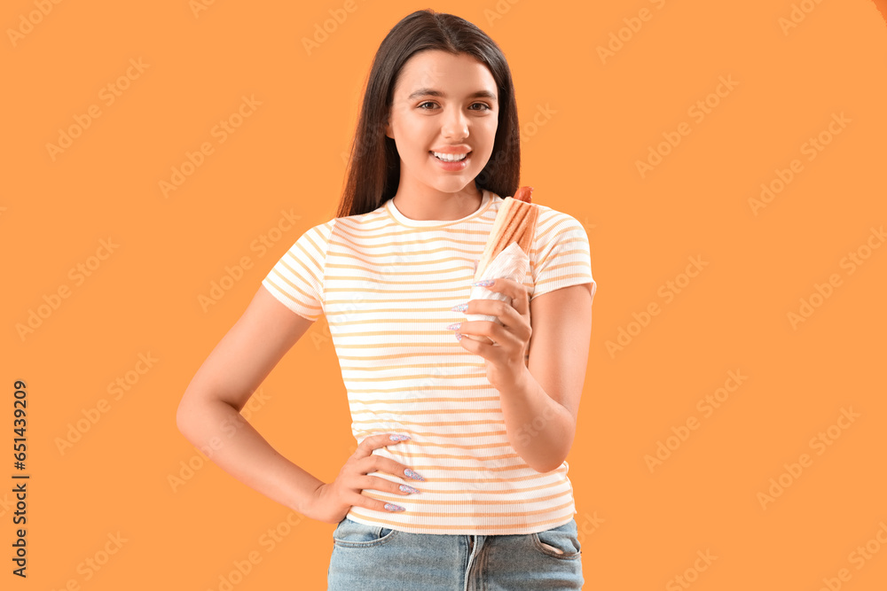 Pretty young woman with tasty french hot dog on yellow background