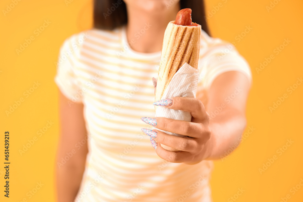 Young woman with tasty french hot dog on yellow background, closeup