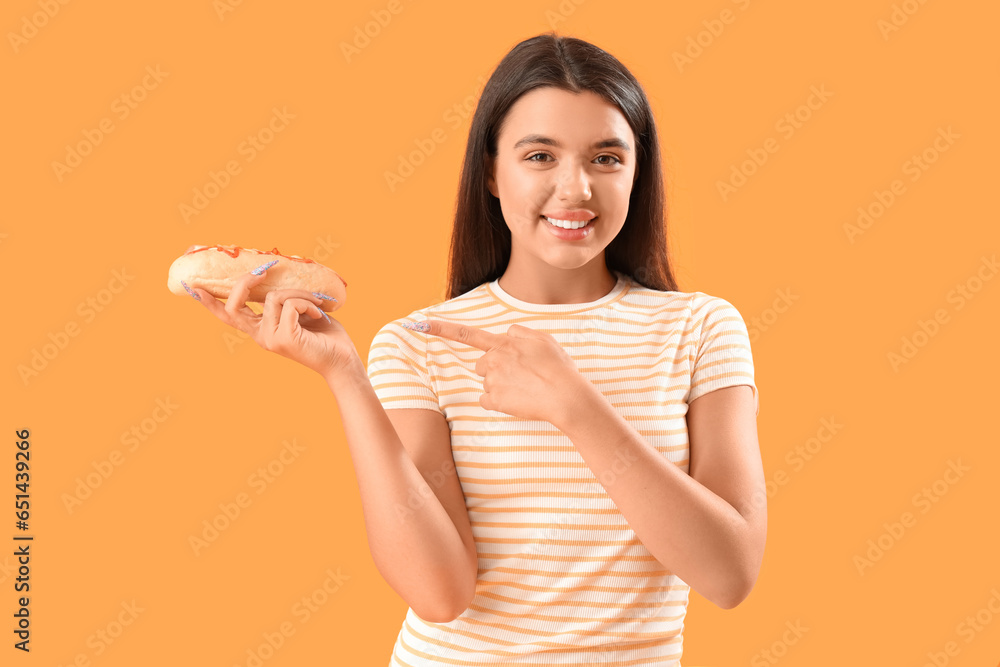 Pretty young woman pointing at tasty hot dog on yellow background