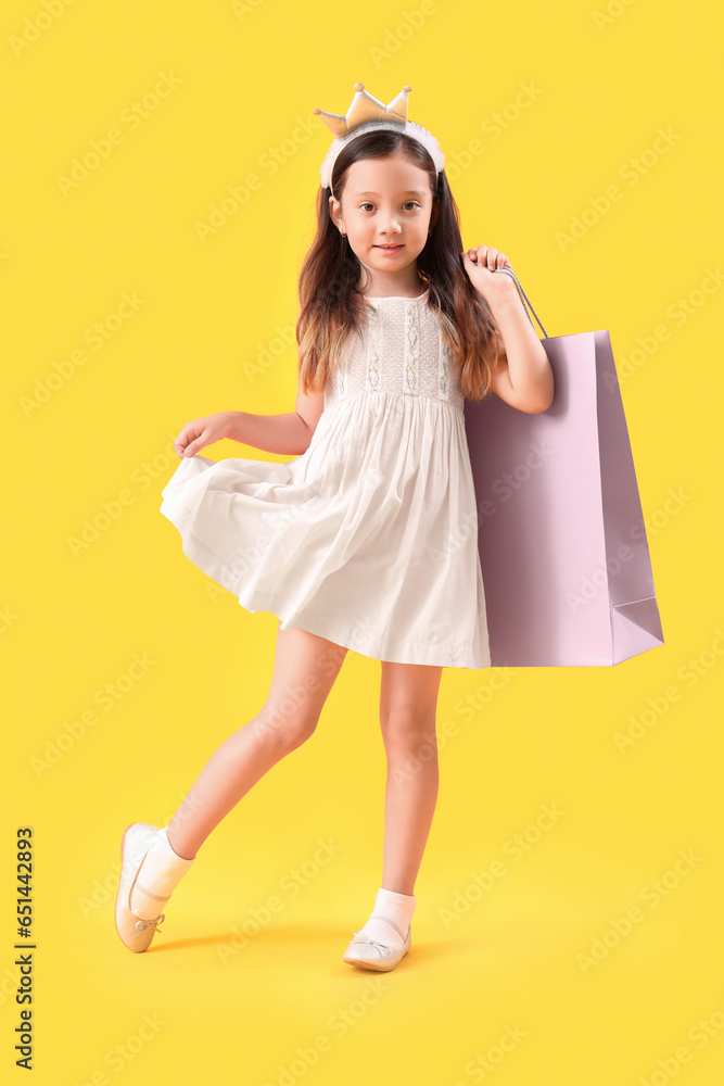 Cute little girl with shopping bag on yellow background