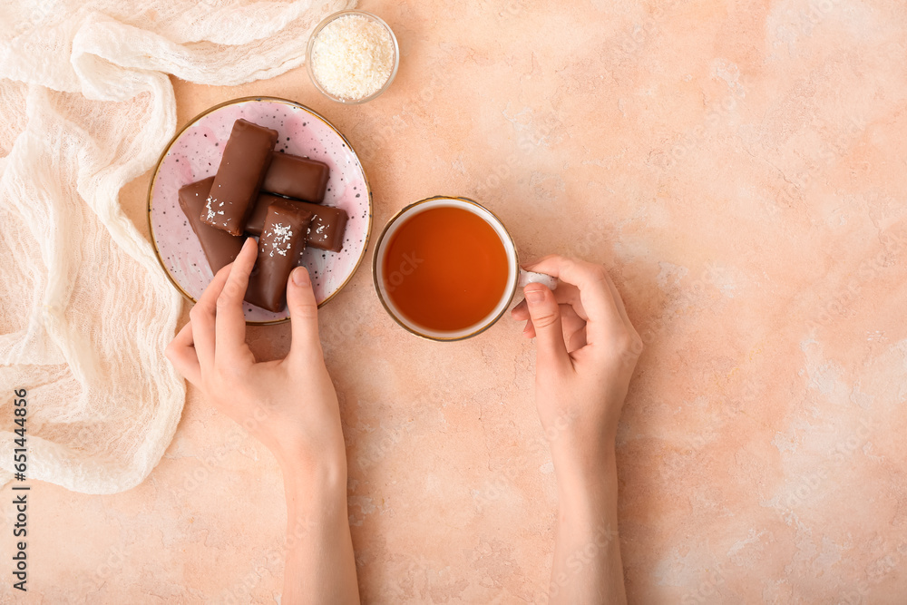 Woman eating tasty chocolate covered coconut candies and drinking tea on beige background