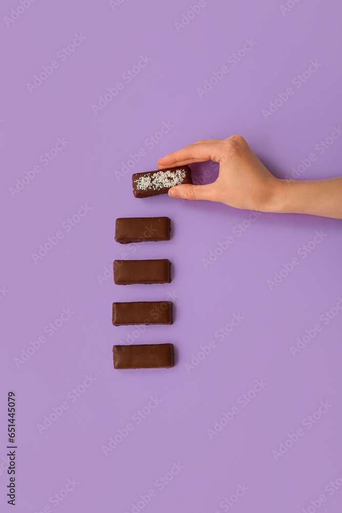 Woman taking tasty chocolate covered coconut candy on lilac background