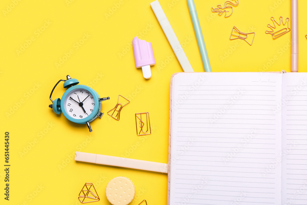 Notebook with different stationery supplies on yellow background