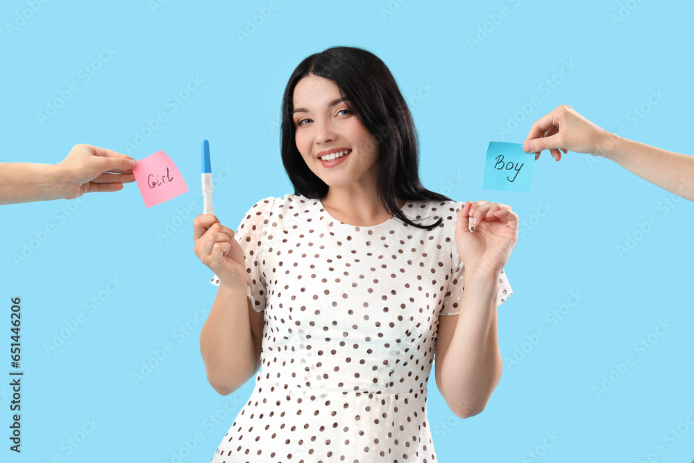 Happy young woman with pregnancy test and hands holding stick notes with text BOY and GIRL on blue background