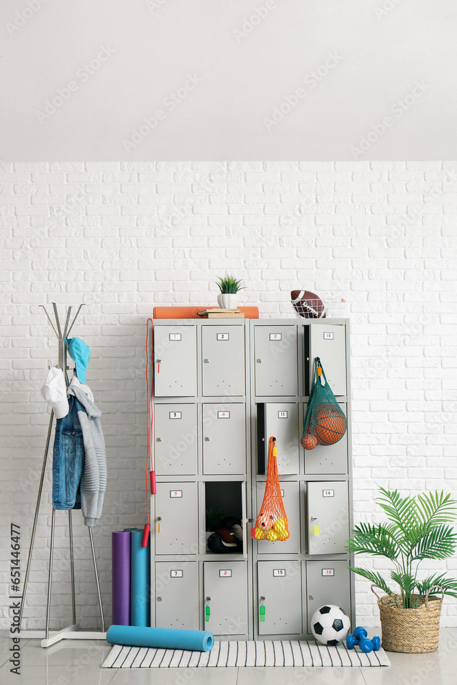 Modern locker with sports equipment near white brick wall