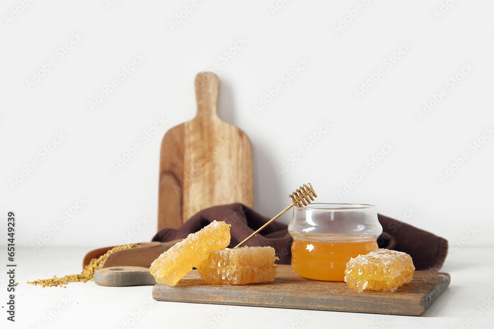 Wooden board with jar of tasty honey and combs on light background