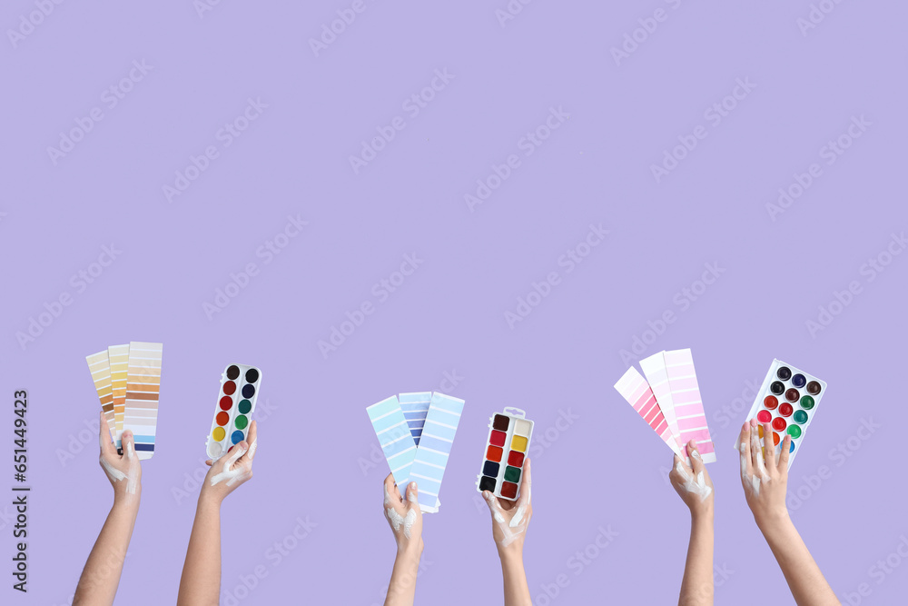 Female hands with color samples and watercolor paints on lilac background