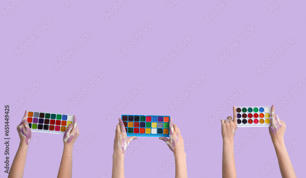 Female hands with watercolor paints on lilac background