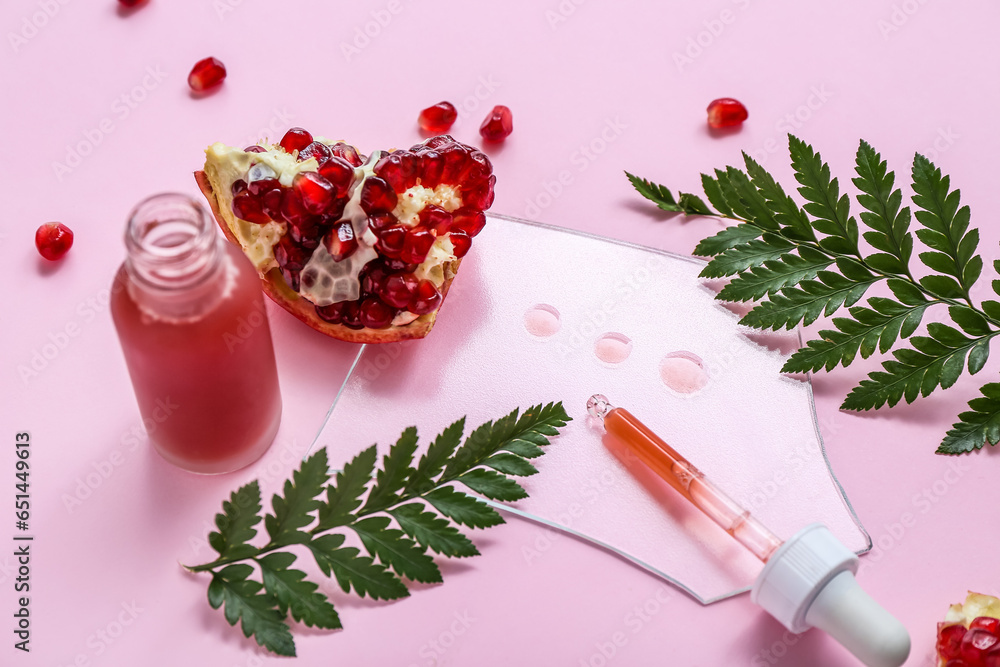 Composition with bottle of essential oil, pomegranate and fern leaves on pink background