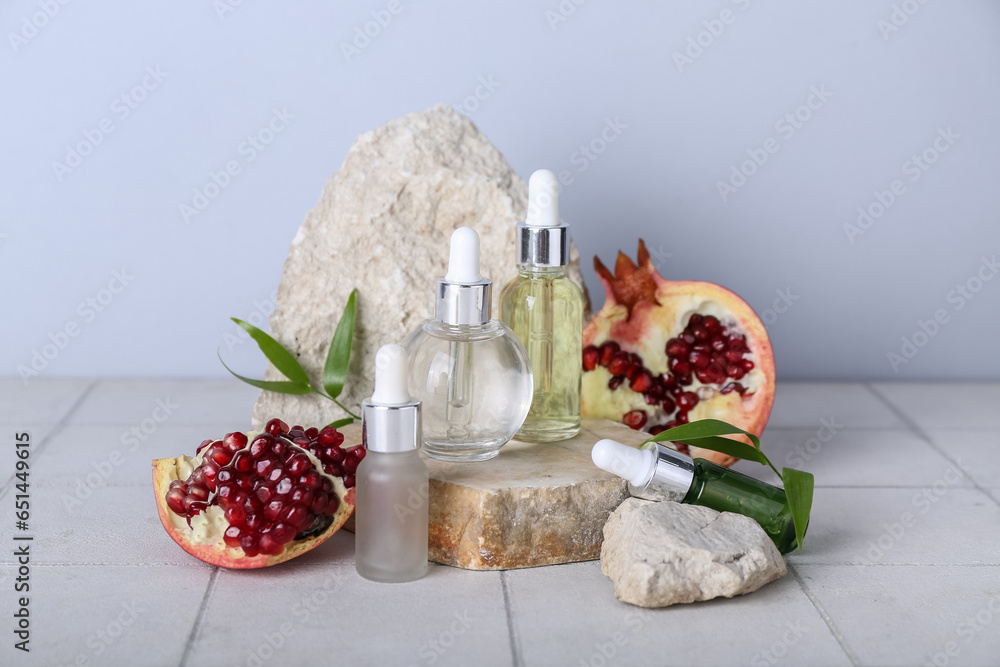 Composition with bottles of essential oil, pomegranate and stones on light tile table