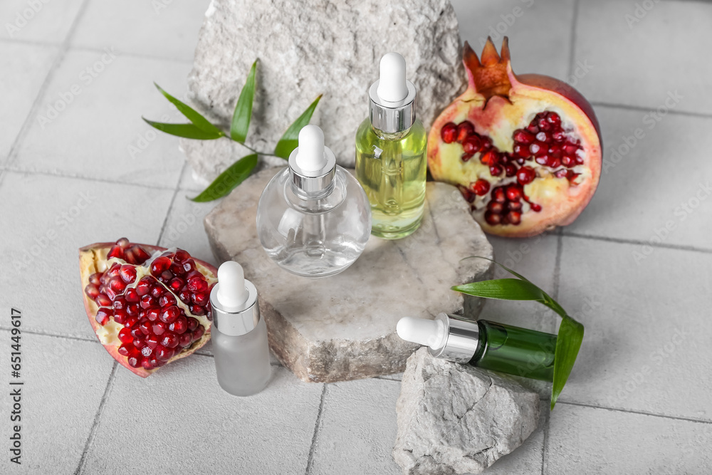 Composition with bottles of essential oil, stones and pomegranate on light tile table