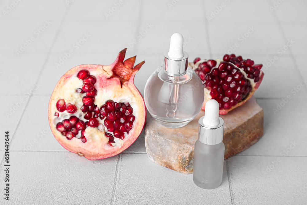 Composition with bottles of essential oil, stone and pomegranate on light tile table