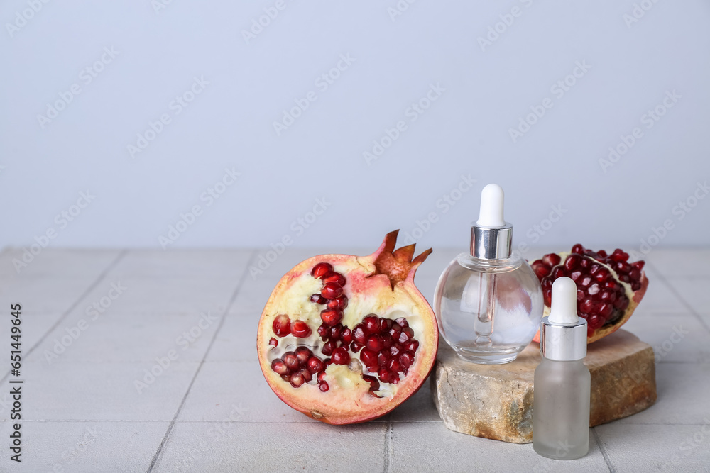 Composition with bottles of essential oil, pomegranate and stone on light tile table