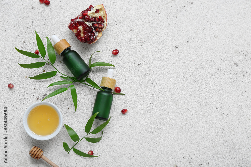 Composition with bottles of essential oil, pomegranate and honey on light background