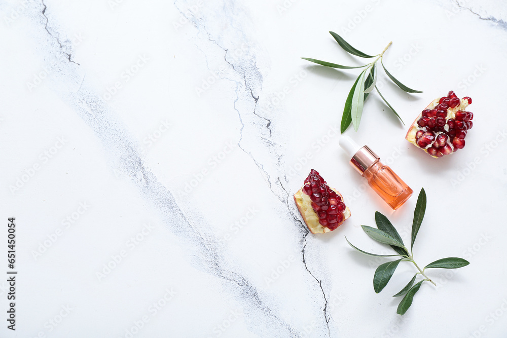 Composition with bottle of essential oil, plant branches and pomegranate on light background