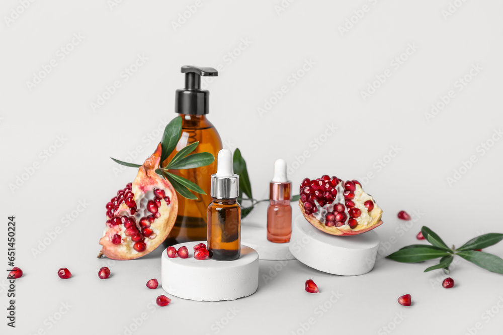 Composition with cosmetic products, pomegranate and plant branches on light background