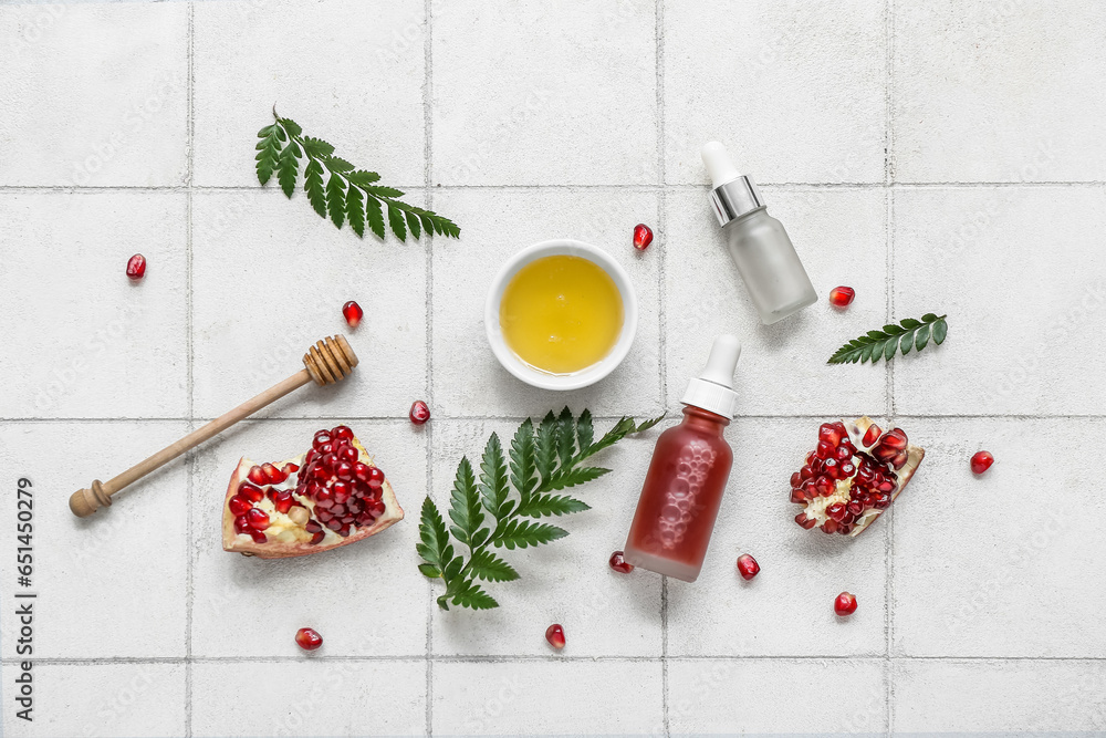 Composition with bottles of essential oil, honey, pomegranate and fern leaves on light tile background