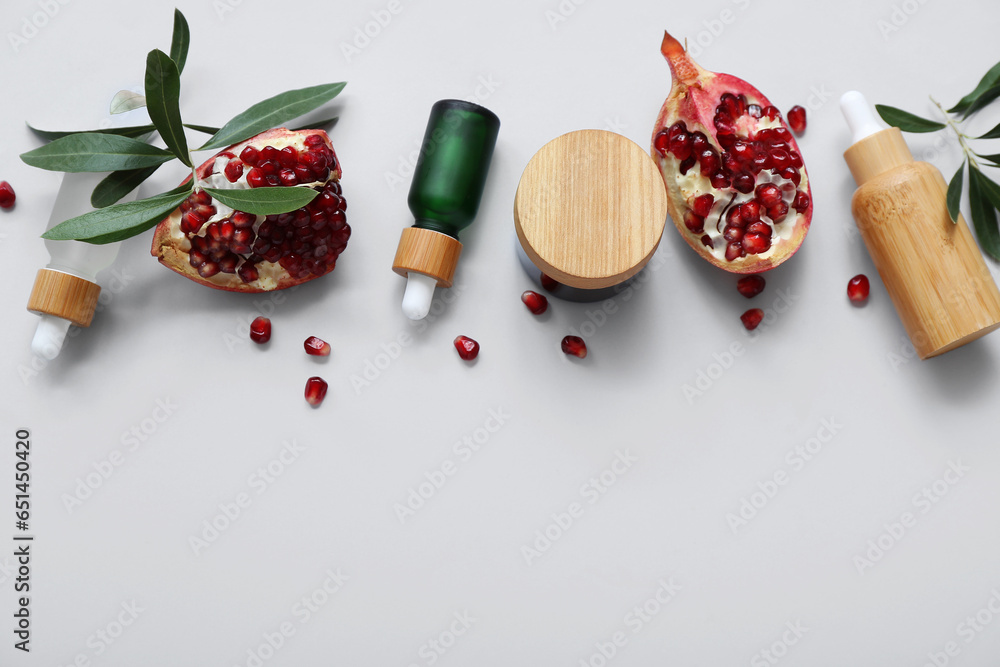 Composition with cosmetic products ripe pomegranate and plant branches on light background