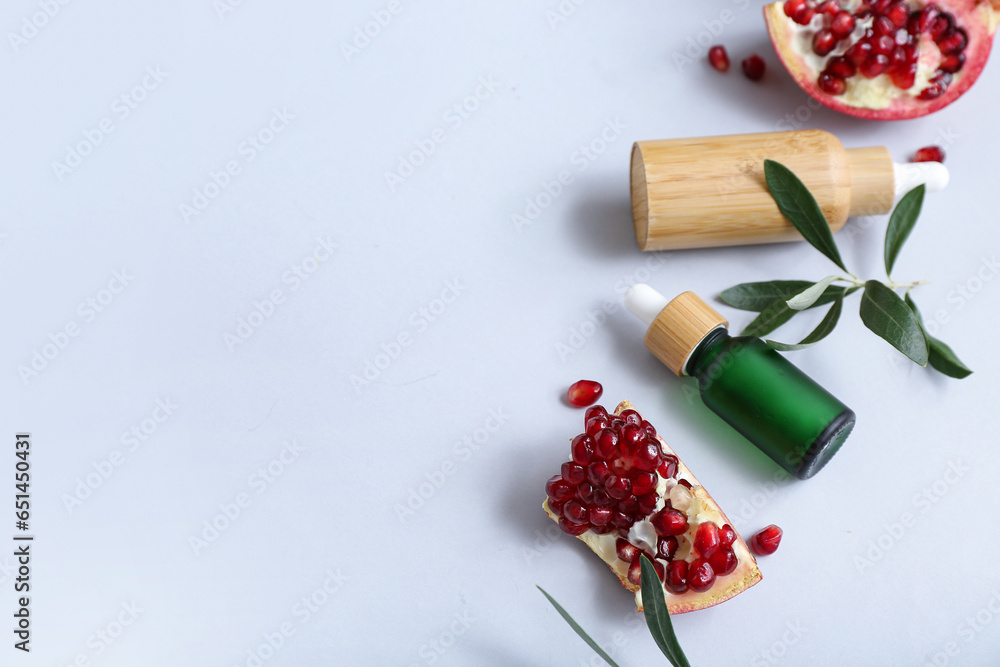 Composition with bottles of essential oil and ripe pomegranate on light background