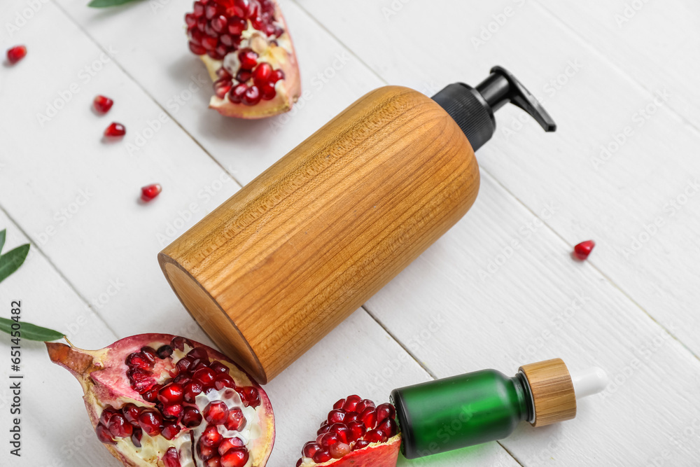 Bottles of cosmetic products and ripe pomegranate on light wooden background, closeup