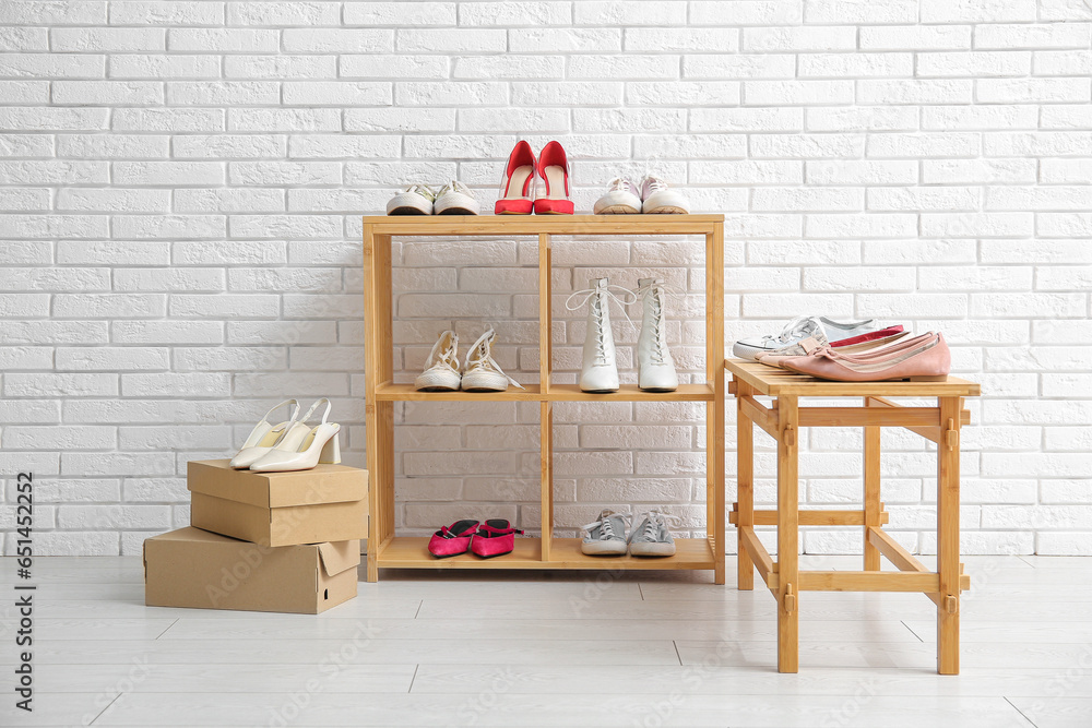 Wooden shelving units with stylish female shoes near light brick wall in store