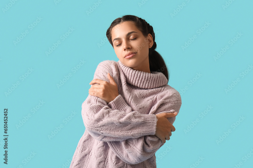 Young brunette woman hugging herself on blue background