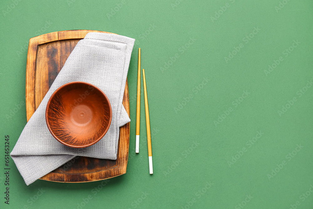 Chinese bowl with chopsticks, napkin and wooden board on green background