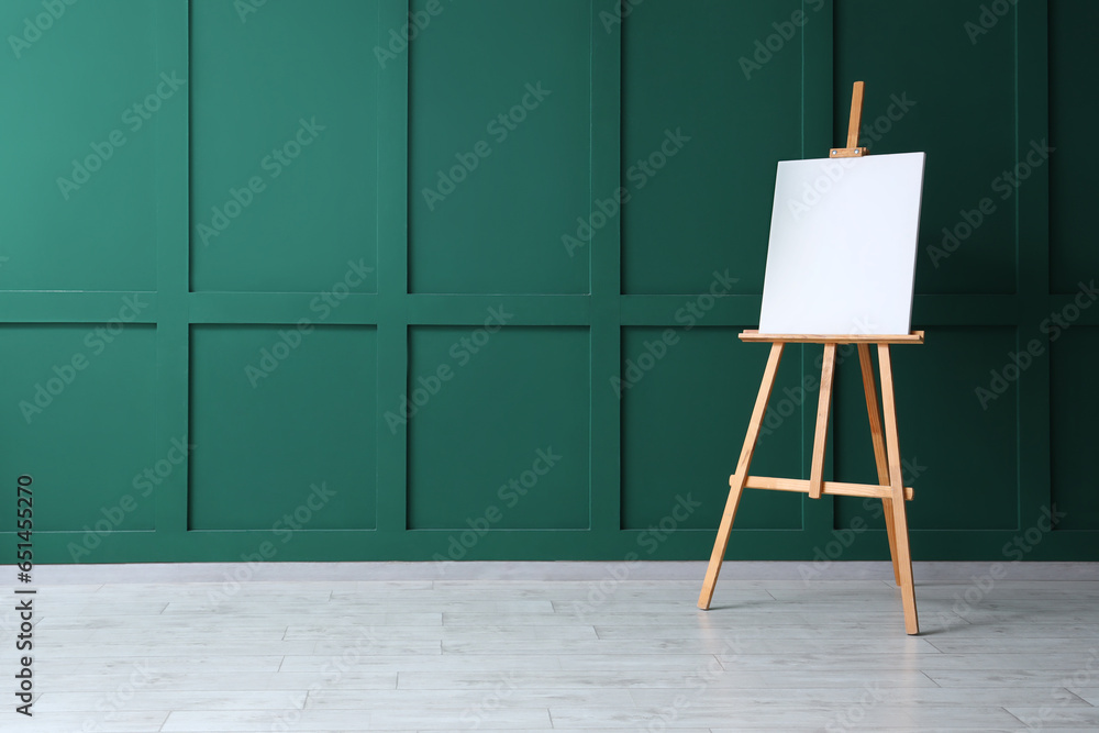 Wooden easel with blank canvas near green wall