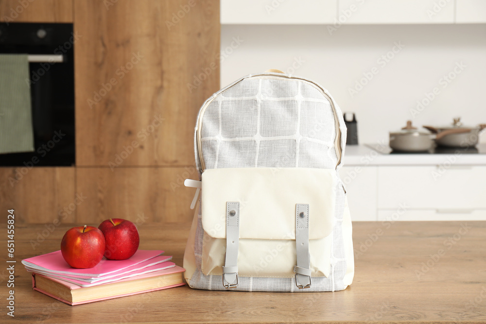 Stylish school backpack with stationery and fresh apples on table in kitchen