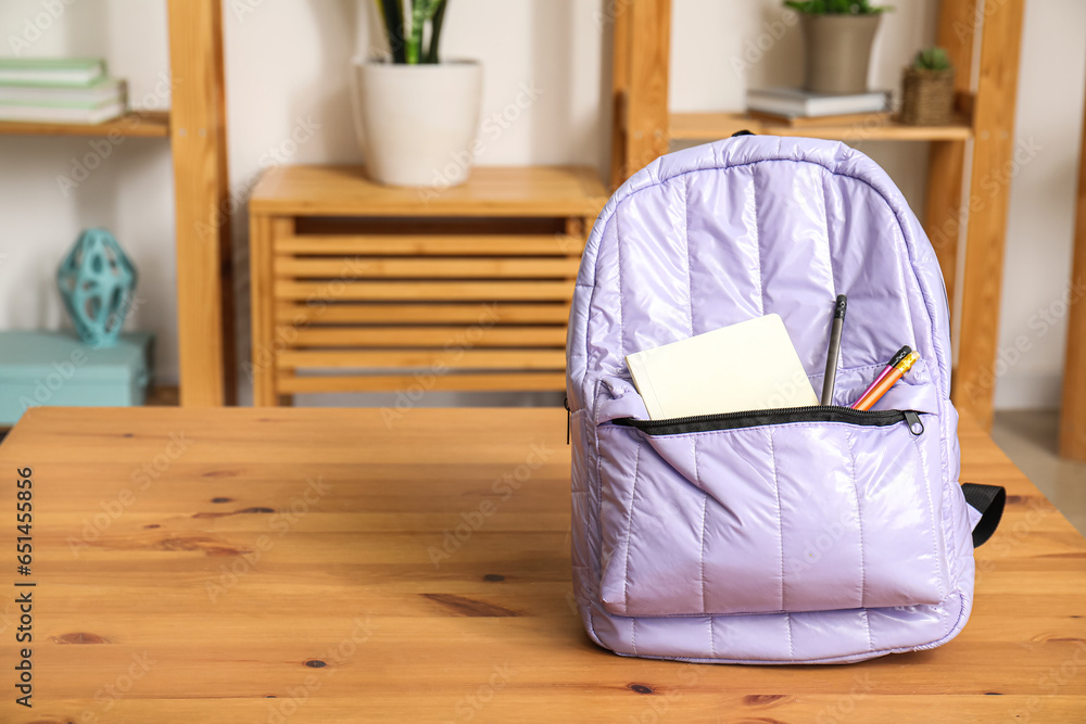 Stylish school backpack with stationery on wooden table in living room