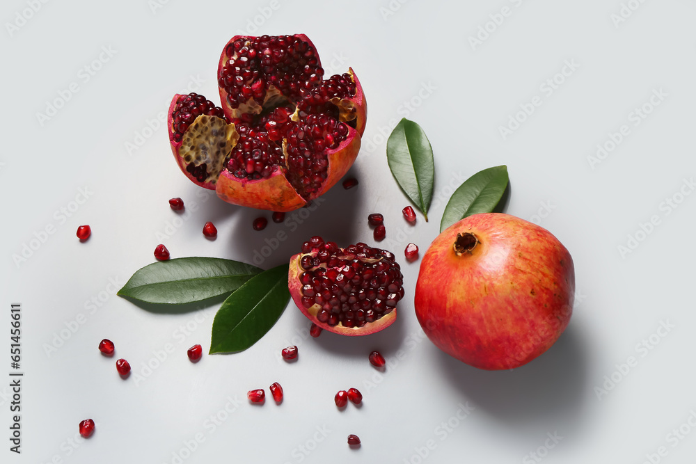 Fresh pomegranates with seeds and leaves on grey background