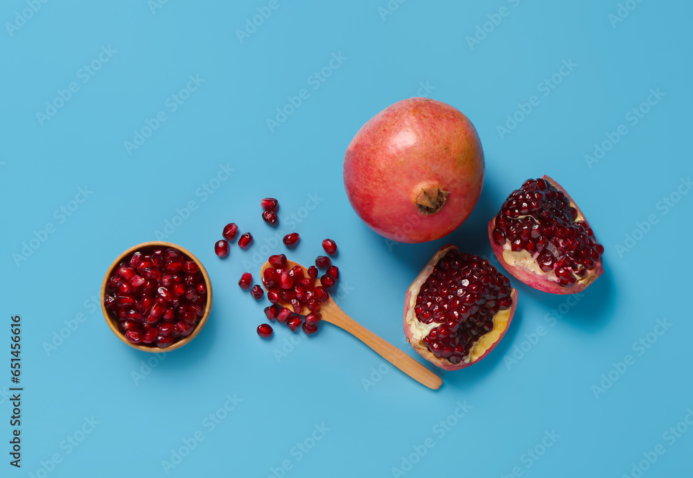 Fresh pomegranates and bowl with seeds on blue background