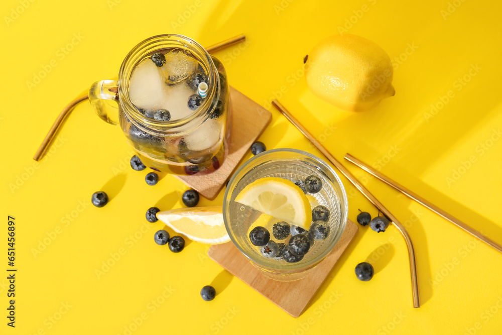 Glass and mason jar of fresh blueberry lemonade on yellow background