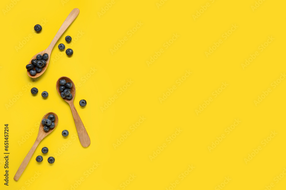 Wooden spoons with fresh blueberries on yellow background