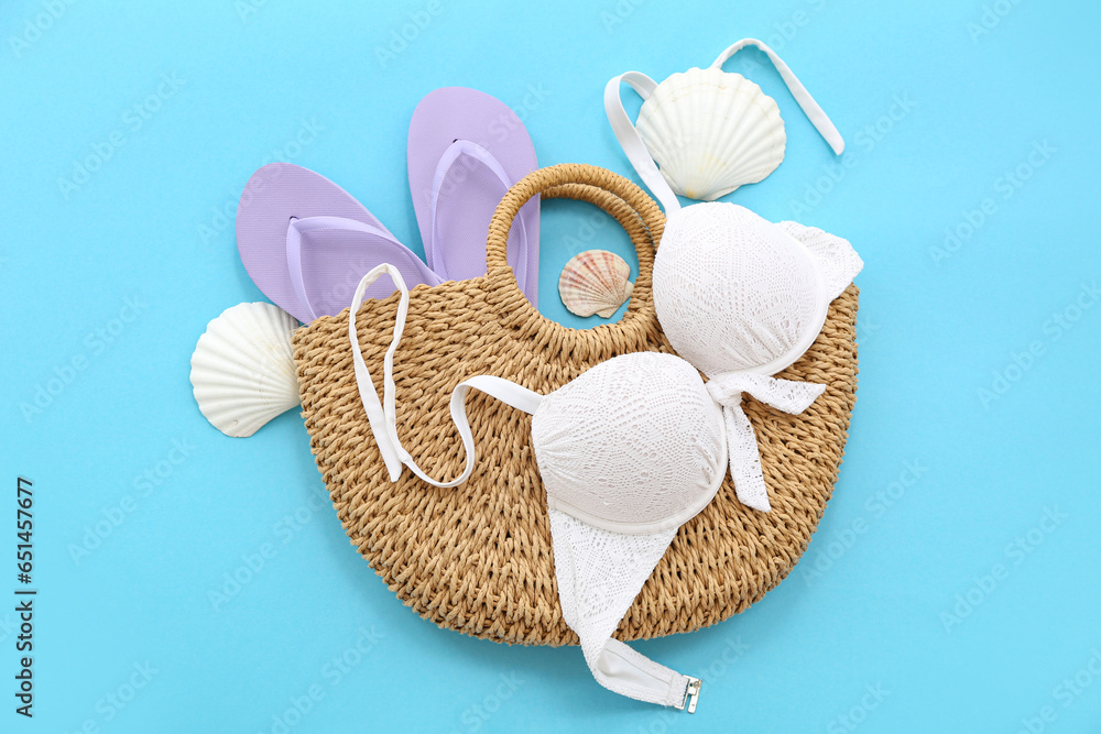 Pair of purple flip flops with swimsuit and straw bag on blue background