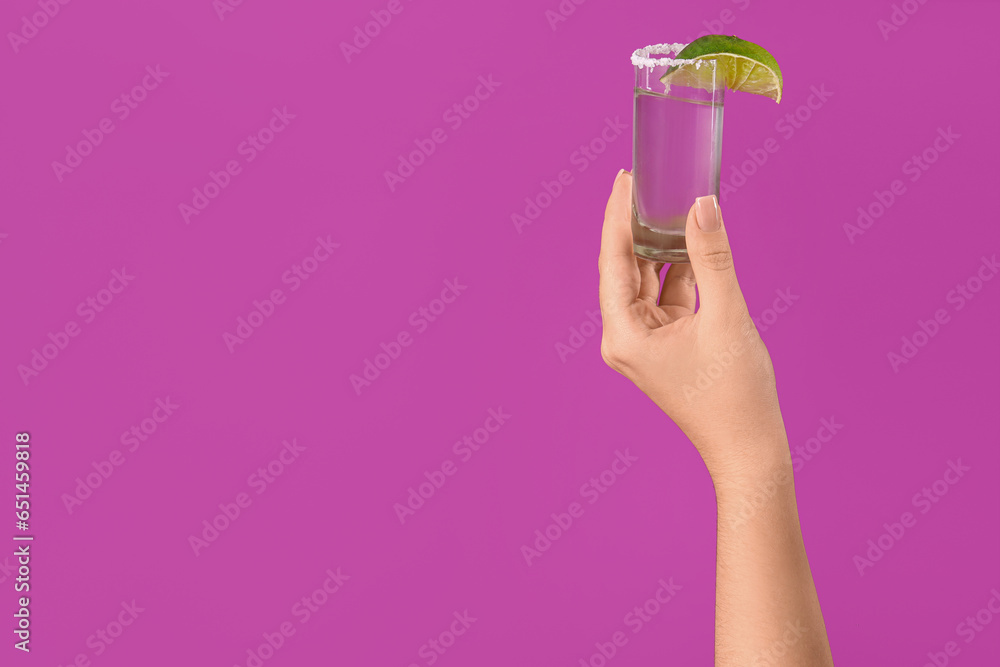 Female hand with shot of tequila on purple background