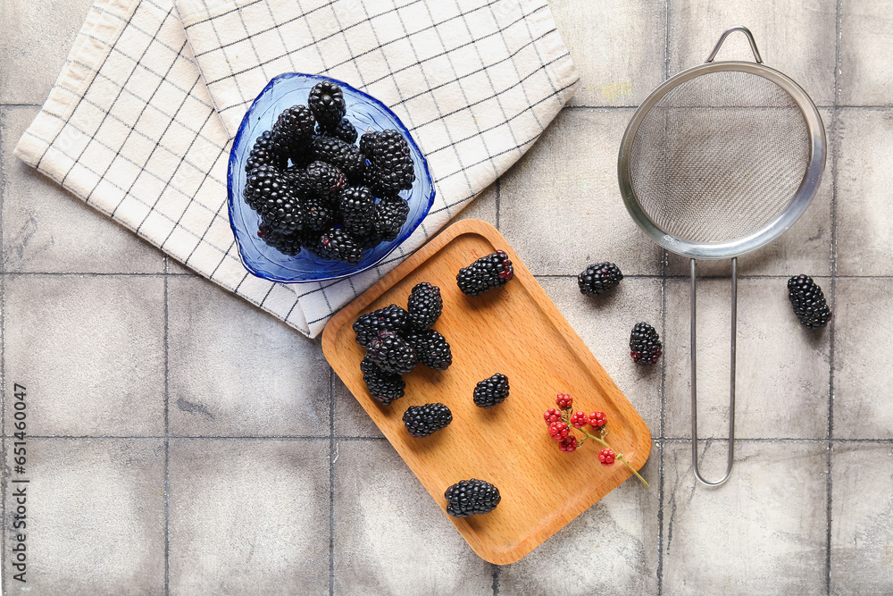 Wooden board and bowl with fresh blackberries on grey tile background