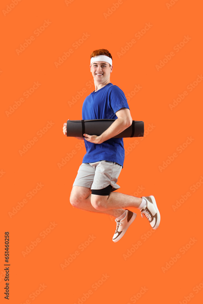 Sporty jumping young man with yoga mat on orange background