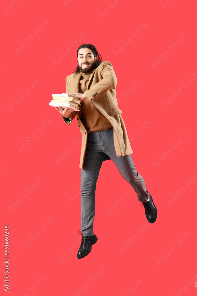 Jumping young man with books on red background