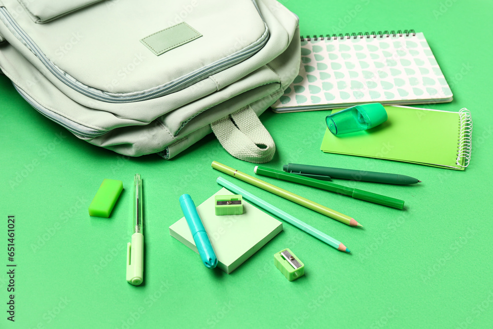 Stylish school backpack with different stationery supplies on green background